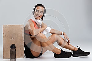 Strong young sports woman isolated indoors with towel on neck listening music with headphones.