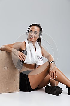 Strong young sports woman isolated indoors with towel on neck listening music with headphones.