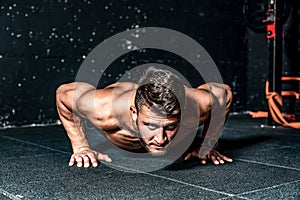Strong young toned muscular fitness man push ups workout training on the gym floor