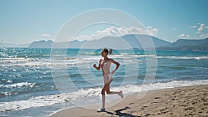 strong young woman running on stormy beach sprinting fast exercising cardio workout training focused female athlete