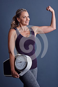 Stronger than I was yesterday. Studio portrait of an attractive mature woman holding a weightscale and flexing against a