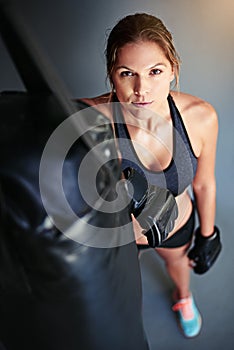 Stronger than your average chick. Portrait of a female boxer leaning against a punching bag.