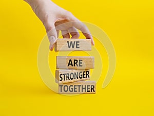 We are stronger together symbol. Wooden blocks with words We are stronger together. Beautiful yellow background. Businessman hand