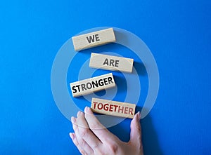 We are stronger together symbol. Wooden blocks with words We are stronger together. Businessman hand. Beautiful blue background.