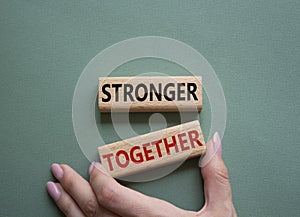 Stronger together symbol. Wooden blocks with words Stronger together. Businessman hand. Beautiful grey green background. Stronger