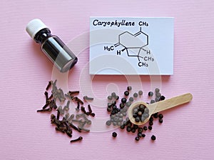 Structural chemical formula of caryophyllene, clove essential oil glass bottle, clove grains and peppercorns on pink background