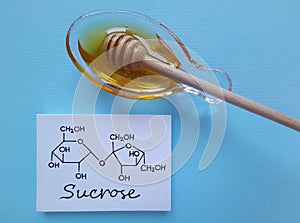 Structural chemical formula of sucrose with a bowl of honey. Sucrose occurs naturally in honey, alternative to refined sugar