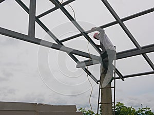 A structural steel worker climbing a ladder onto a high rooftop to do a house roof structure installation