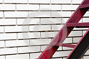 Part of the stairs red metal ladder leading up against of a white brick wall