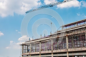 Structure of large building with worker working, crane and scaffold in construction site