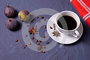 On a structured background stands a cup of coffee, coffee beans, anise and figs