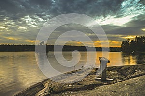 Structured blue cloud on a countryside lake during the sunset on a wooden bench through the orange horizon in beatiful summer day