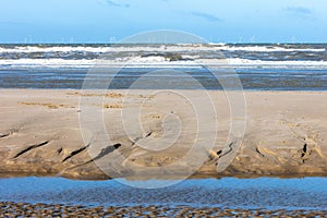 Structures in the sand on a beach of the North sea, with a rough sea with spindrift waves