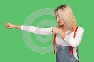 Struggle with threat. Side view of brave self-confident adult blond woman in denim overalls boxing and fighting