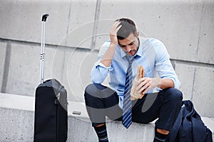 Struggling with retrenchment. A young businessman sitting outdoors and drinking while looking dejected.