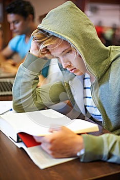 Struggling to get through the wor. A young student reading from his textbook during class.