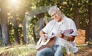 Strumming away. a handsome mature man playing the guitar while camping in the woods.