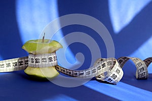 Stub of a green apple with a centimeter tape on a blue background