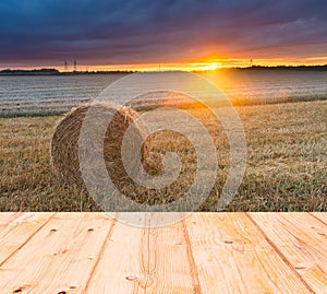 Stubble field at sunset with old wooden planks floor on foreground