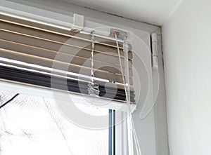 Stuck blinds.Adjusting the white blinds in height use a cord.Half-open metal blinds mounted on a plastic window.