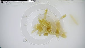 Stuck together cheap tasteless pasta thrown into boiling water, shot in slow motion on white background,