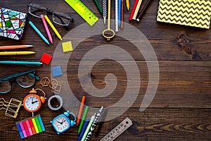 Student accessories. School or student`s stationery mockup with glasses, alarm clock, notebook on dark wooden background