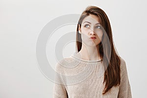 Student is bored making up ideas what to do. Portrait of carefree dreamy caucasian girl looking up with puckered lips