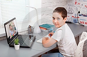 Student boy with laptop having video call with teacher online at home