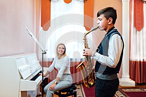 A student boy in a saxophone lesson learns to play accompaniment of a cheerful teacher on the piano