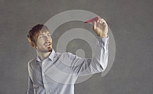 Student or businessman holding red paper plane standing against grey studio background