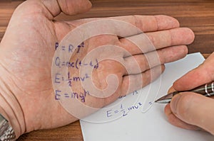 Student is cheating during exam with cheat sheet with formula.