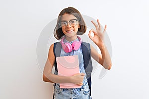 Student child girl wearing backpack glasses book headphones over isolated white background doing ok sign with fingers, excellent