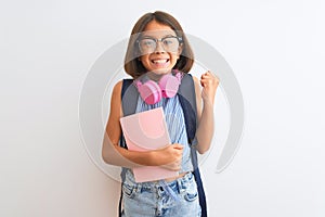 Student child girl wearing backpack glasses book headphones over isolated white background screaming proud and celebrating victory