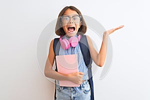 Student child girl wearing backpack glasses book headphones over isolated white background very happy and excited, winner