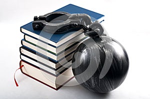 Student debt concept with a stack of books next to a ball and chain symbolizing the burden tuition costs represent isolated on