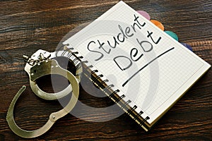 Student debt handwritten sign in notebook and handcuffs.