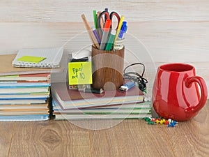 Student desktop, stack books, accessories, stationery, red mug, flash drives, crayons, on wooden table