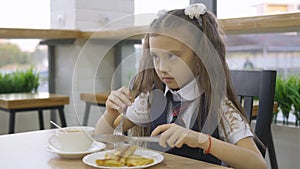 Student elementary school in a school uniform sitting at a table in the school cafeteria and eat.