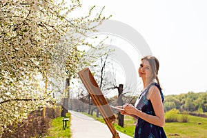 Student girl artist painting landscape in the open air in early spring.