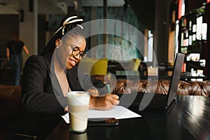 Student girl browsing Internet, using free wi-fi at cafe. African freelancer thinking on ideas for her blog, using laptop at co-