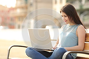 Student girl browsing a laptop sitting in a bench
