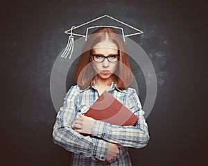 Student girl in cap, glasses and a book at blackboard