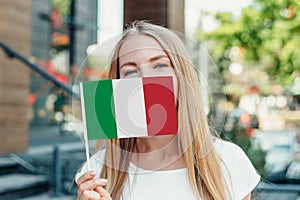 Student girl covers her face with a small italian flag and stands near the university on the street