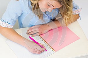 Student girl at desk with notebook and pen writing.