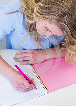 Student girl at desk with notebook and pen writing.