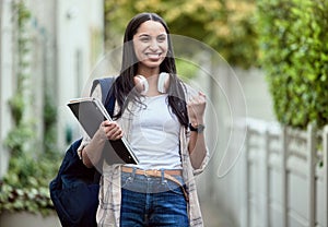 Student, girl and fist pump on campus with smile, headphones and books for learning, development and study. Female