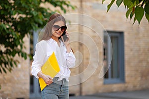 Student girl with a folder in her hands talking on the phone on campus. University studies