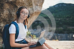 Student girl with glasses enjoying vacation in mount using headphones and laptop studying online education in nature, traveler