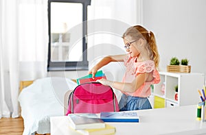 Student girl in glasses packing school bag at home