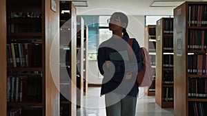 Student girl holding digital tablet and walking between shelves in library.Education and learning concept